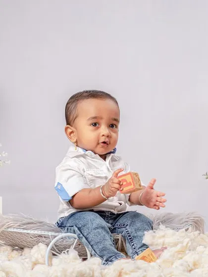 A classic 'sitter session' portrait, designed to celebrate the milestone of a baby sitting up independently. The clean, white setup with floral accents keeps the focus entirely on the baby's proud achievement and sweet expression.