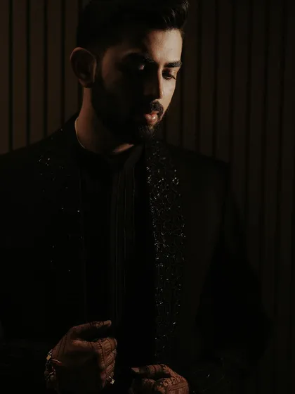 A close-up, moody portrait of the groom. The low-key lighting focuses on the details of his embroidered collar and his intense expression, creating a powerful and sophisticated image.