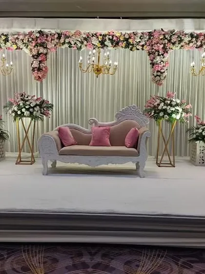 An elegant stage setup with a pink and white color scheme. The design features beautiful chandeliers and classic white pillars, perfect for a formal engagement or reception.