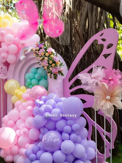 A giant butterfly wing prop adorned with a cascade of pastel balloons and flowers, part of Ayra's rainbow butterfly theme.