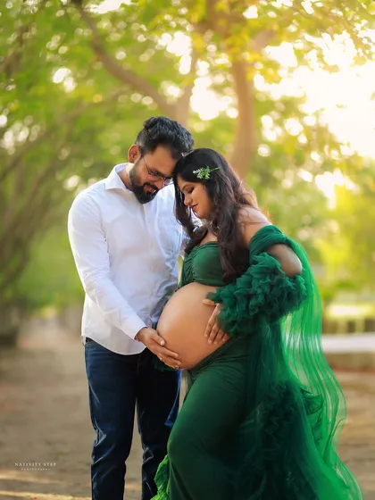 An intimate outdoor portrait of a couple. The focus is on their connection and the shared moment of holding the baby bump.