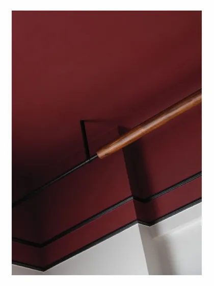 To avoid a false ceiling, we designed this custom lighting solution where a wooden rod wraps around a metal rod. It provides a source of indirect light, casting a dim glow onto the Marsala-colored ceiling and acting as a minimalist sculptural piece.