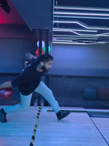 A focused player is captured in motion, about to release a red bowling ball. The "AIR HOCKEY" neon sign is visible in the background, showing the variety of games nearby.