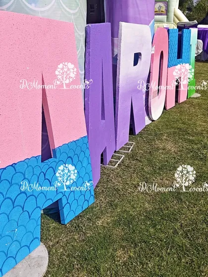 A close-up of the custom-painted marquee letters for the mermaid theme. The letters feature a gradient of pink and purple with a blue mermaid scale pattern at the bottom.