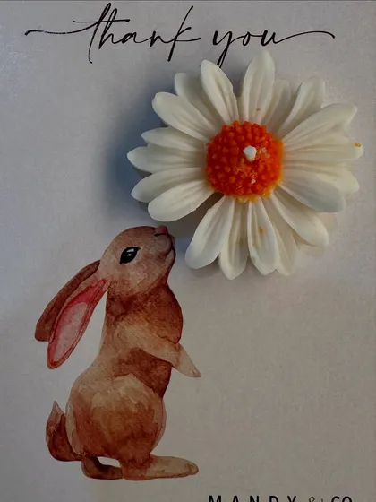 The orange and white daisy candle paired with a cute bunny-themed card, a gift that smells like rose and looks like sunshine.