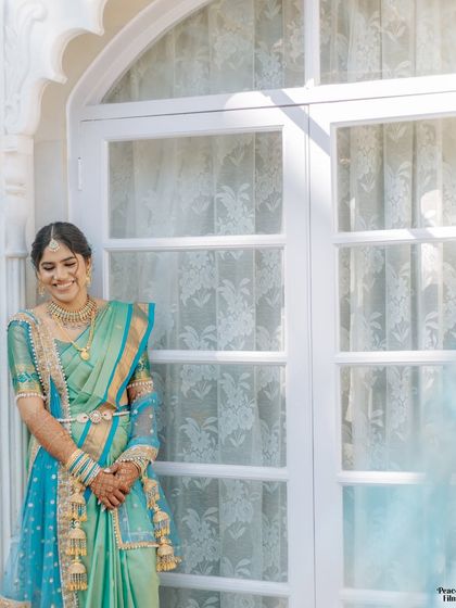 A serene portrait of the bride in her beautiful turquoise and green saree, her gentle smile captured in the soft morning light.
