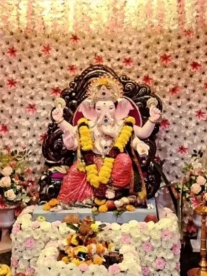 This Ganpati setup features a beautiful backdrop made of star-shaped white flowers, creating a unique texture. The idol is placed on a base decorated with matching flowers for a cohesive look.