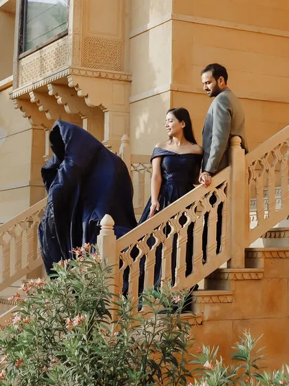 A moment of regal elegance on the steps of a Jaisalmer palace. The bride's flowing blue gown cascades down the stairs, creating a sense of drama and luxury that befits the royal setting.