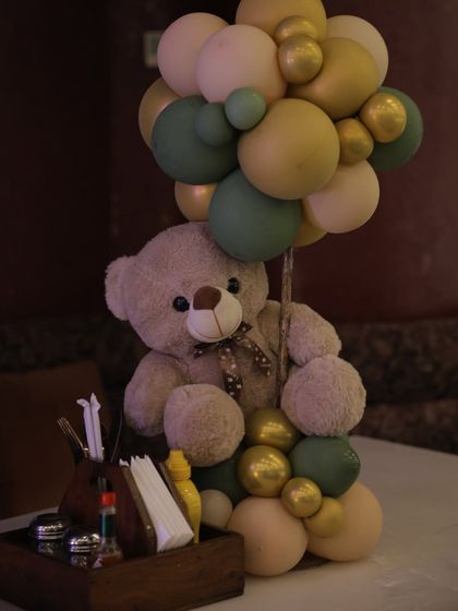 A detailed shot of a teddy bear table centerpiece. The soft colors of the balloons and the cute bear create a charming focal point for guest tables.