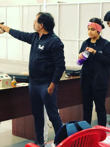 Coaching is an interactive process. Here, a coach observes a shooter's form during a competition, providing real-time feedback and support to ensure peak performance.