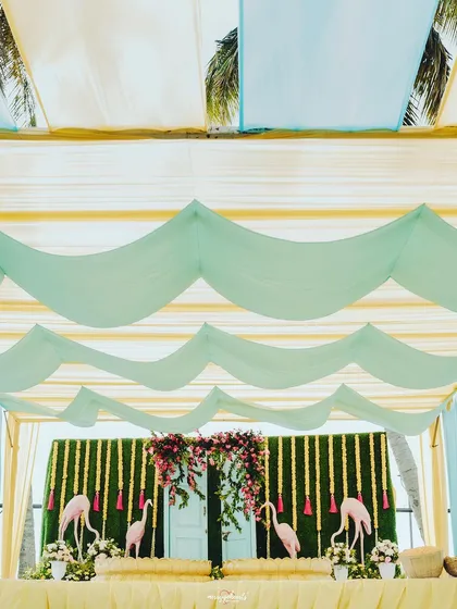 A closer look at the flamingo-themed stage backdrop, with a wall of greenery and hanging marigold strings.