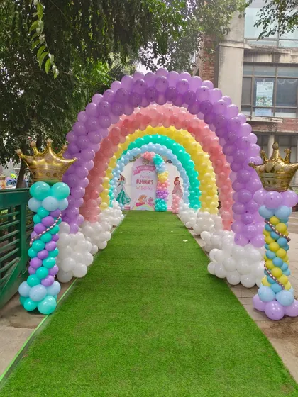 A magnificent rainbow balloon arch creating a tunnel entrance on a green lawn for a magical princess party.