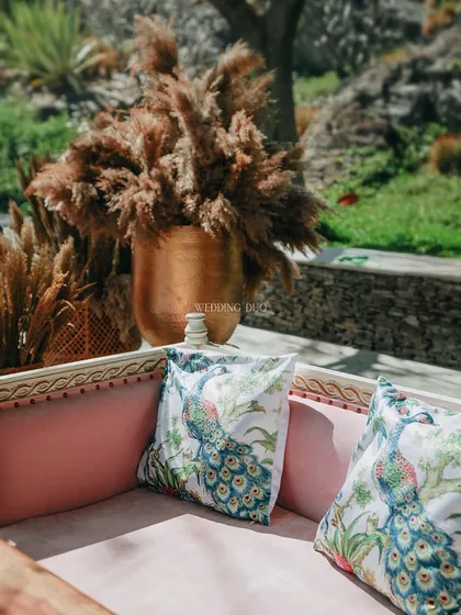 It's the little details that make a day unforgettable. For this event, we used custom-printed peacock cushions on a pink velvet sofa, set next to a large brass vase fatores pampas grass.