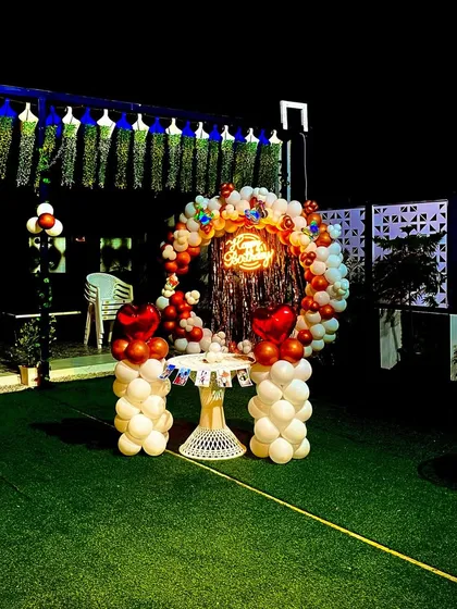 A beautiful birthday setup on an open terrace. This features a circular balloon arch with a shiny backdrop and a neon sign, perfect for cake cutting and photos.