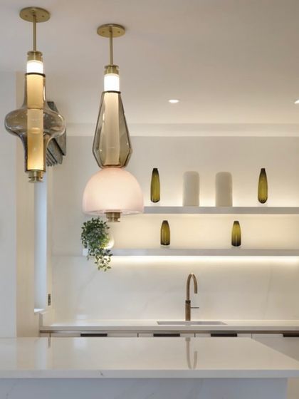 Two different Luna Kaleido pendants are paired over a kitchen counter, showcasing the mix-and-match possibilities of the collection. The combination of shapes and colors creates a personalized and artistic statement.
