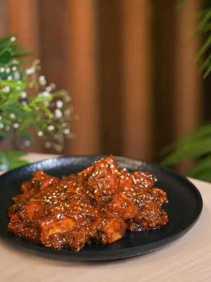 A spicy chicken appetizer, tossed in a thick red sauce and sprinkled with sesame seeds. This behind-the-scenes shot shows the dish just after it's been cooked.