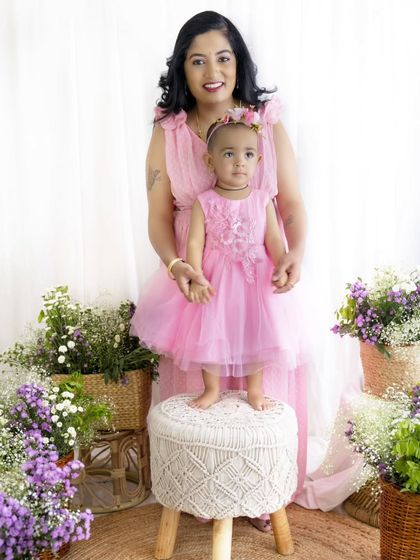 A proud mother stands with her daughter, who is standing on a macrame stool. A sweet pose that shows how much she has grown.
