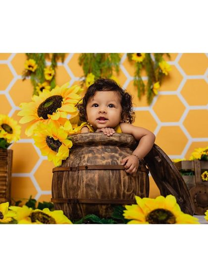 A playful baby peeks out from a rustic wooden barrel amidst a field of sunflowers in our studio. This creative composition adds a touch of whimsy and fun to the baby portrait session.