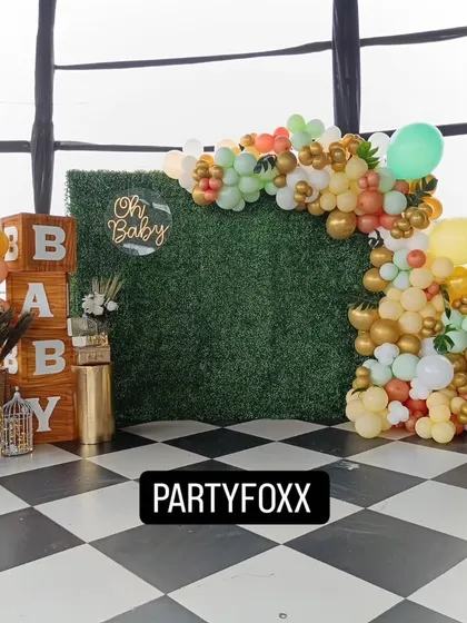 A modern and rustic baby shower setup featuring a green foliage wall, a neon "Oh Baby" sign, and large wooden "BABY" blocks. This elegant design is perfect for a chic celebration.