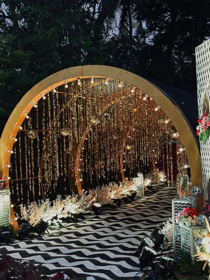 A glamorous Sangeet entrance featuring a tunnel of shimmering gold strings and disco balls, leading to a black-and-white chevron patterned walkway.