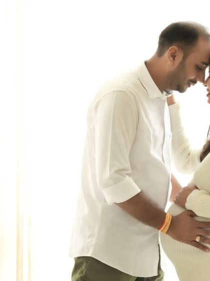 A beautifully simple and intimate black and white portrait. The high-contrast lighting emphasizes their connection and the silhouette of the baby bump.