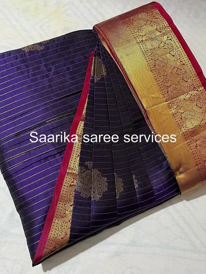 A deep purple saree with gold stripes, folded and ready for a customer.