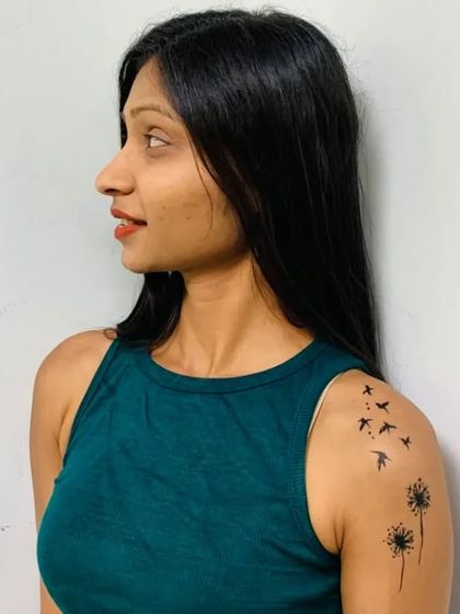 An elegant temporary tattoo of dandelions turning into birds, painted on the shoulder.