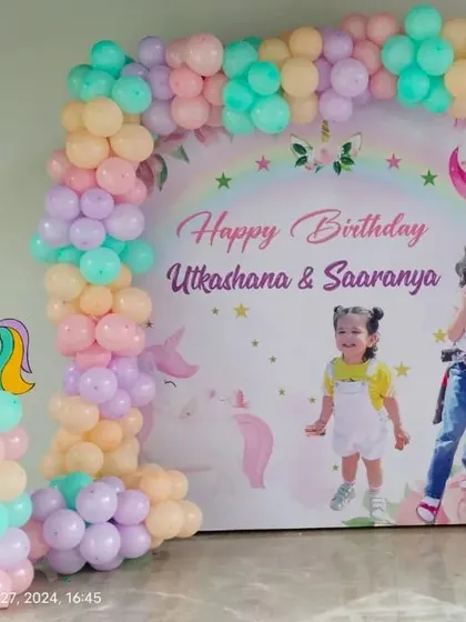 A personalized unicorn theme backdrop featuring photos of the birthday girls. This setup combines a pastel balloon arch with custom unicorn cutouts for a unique and memorable photo booth.