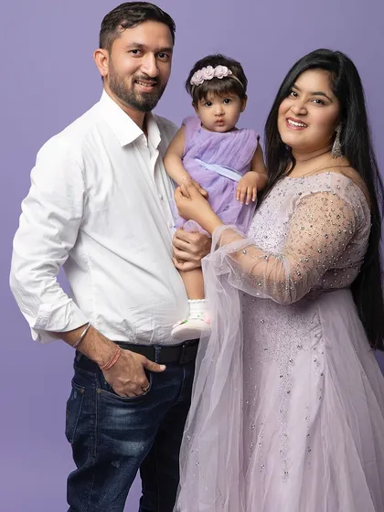 A classic family portrait against a simple lavender background. The focus is entirely on their happy faces and the love they share.