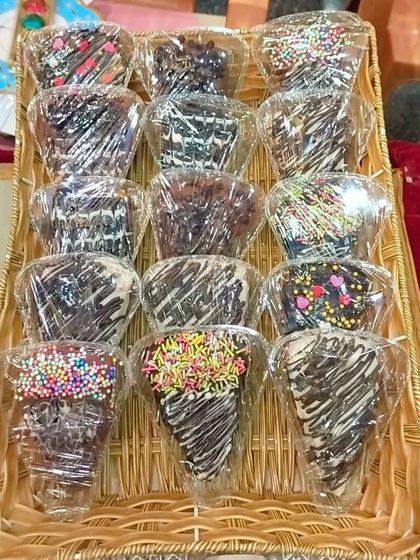 These are my cone-shaped chocolate pastries, all wrapped up and ready for an event. They are filled with cake and cream, dipped in chocolate, and finished with sprinkles.