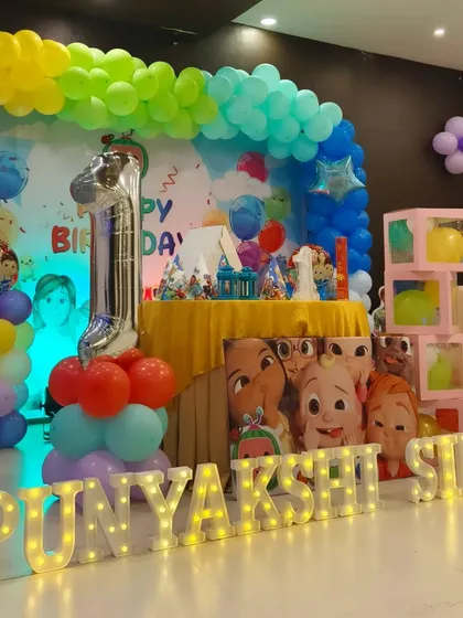The full Cocomelon stage setup for Punyakshi's first birthday, complete with marquee letters, character cutouts, and a colorful balloon backdrop.