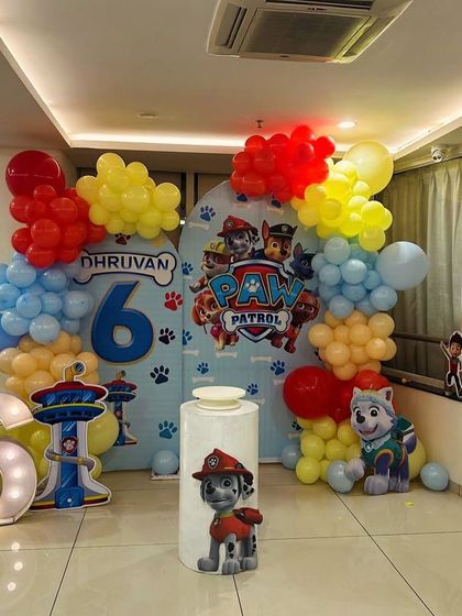 A full view of a Paw Patrol themed setup. This decoration includes a large backdrop, multiple character cutouts, a themed plinth, and a light-up marquee number.