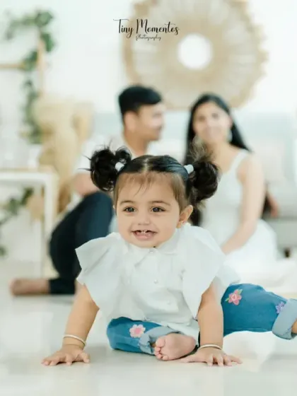 This little girl is the star, crawling towards the camera with a big smile, while her parents look on with love from the background.
