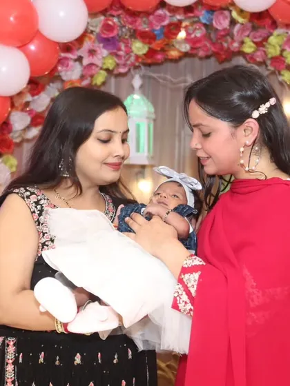 Two women admiring the newborn baby against the festive red and white balloon decor. A sweet, candid shot full of warmth.