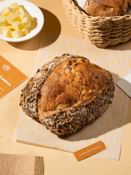 A rustic, seeded loaf of sourdough bread. The styling is simple and natural, letting the quality of the bread speak for itself.