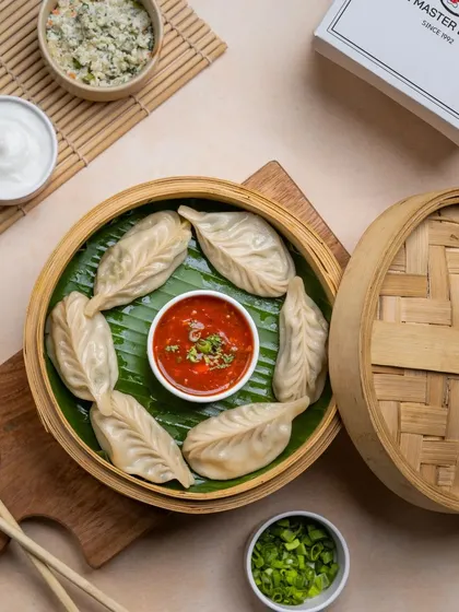 A close-up of our steamed momos, showing the delicate wrapper and the fresh ingredients served alongside, including chopped spring onions and dipping sauces.