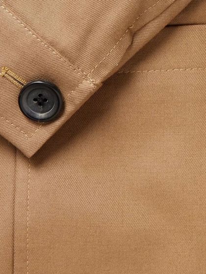 A close-up of a button on a tan jacket, showing the clean stitching of the buttonhole. This is a small but crucial sign of a well-made garment.