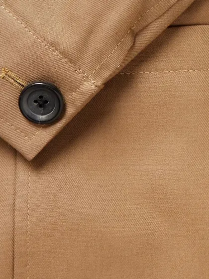 A close-up of a button on a tan jacket, showing the clean stitching of the buttonhole. This is a small but crucial sign of a well-made garment.