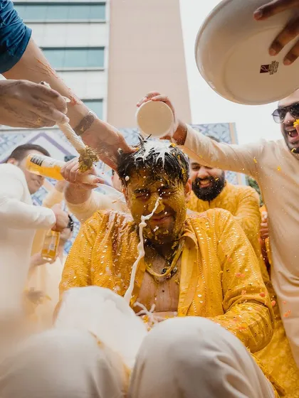 A groom getting a full-on Haldi treatment from his friends, including beer and curd.