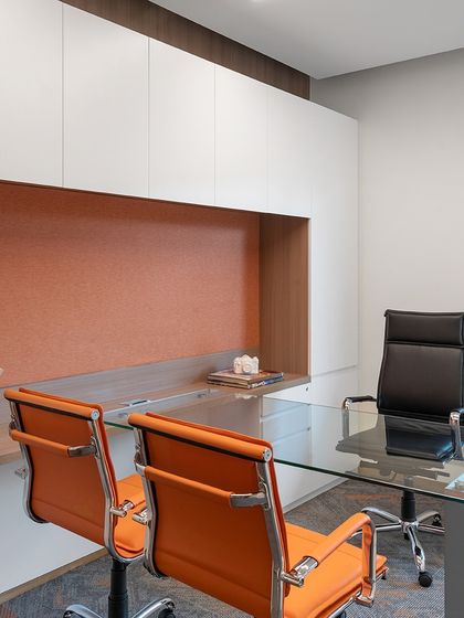 A private cabin in 'The High-Flying Office' features a glass desk and vibrant orange chairs, continuing the brand's color scheme. The space is designed for comfort and functionality, with ample storage and a view of the surrounding greenery.