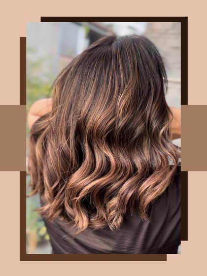 A beautiful shot of a balayage with warm brown and light caramel tones. The hair is styled in soft, beachy waves.