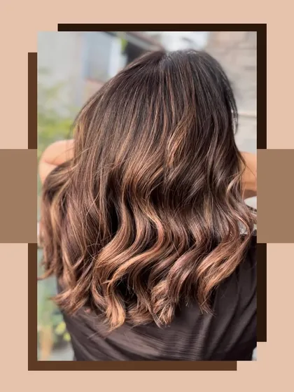 A beautiful shot of a balayage with warm brown and light caramel tones. The hair is styled in soft, beachy waves.