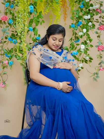A serene portrait of a mother-to-be in a beautiful royal blue gown. The delicate floral backdrop in our studio adds a touch of elegance and softness to the image.