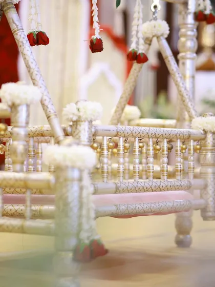 A detailed shot of the ornate silver-coated cradle, adorned with delicate white flowers and hanging red rose buds.