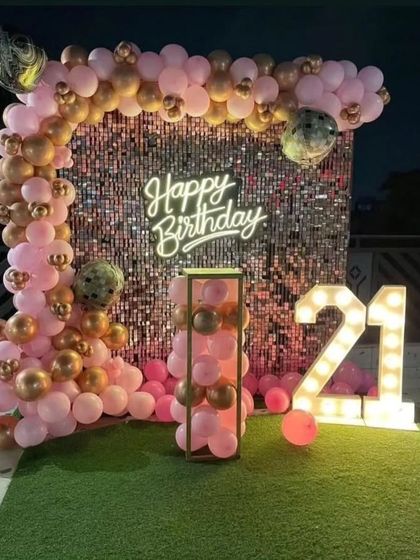 A vibrant 21st birthday setup with a pink sequin wall, a pink and gold balloon arch, and large marquee numbers.