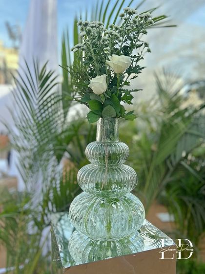 A simple arrangement of two white roses in a stylish ribbed glass vase, demonstrating that beauty often lies in simplicity. This detail is part of the cohesive, eco-luxe design.