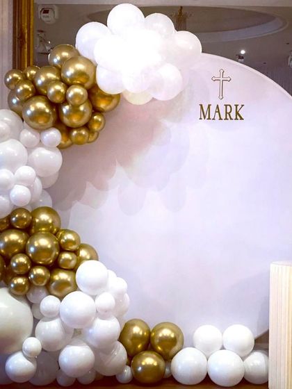 A minimalist and modern First Holy Communion backdrop. The clean white circular panel is accented with a white and gold balloon garland.