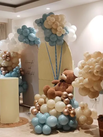 This is an example of how I can transform a living room for a baby shower. I used a soft color scheme of pastel blue, beige, and rose gold to create multiple balloon arrangements, including a large arch and free-standing clouds, all tied together with a cute teddy bear theme.