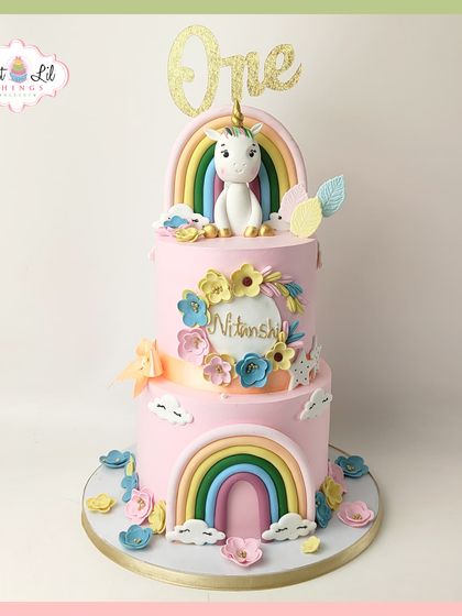A one-derful unicorn and rainbow cake for a first birthday. This two-tiered pink cake is decorated with pastel rainbows, flowers, and a cute unicorn topper, creating a magical centerpiece.