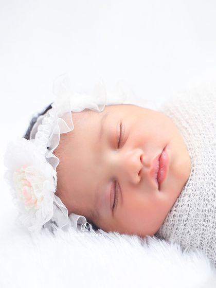 The face of an angel. This close-up in a white floral headband shows the perfect, peaceful expression of a sleeping newborn.